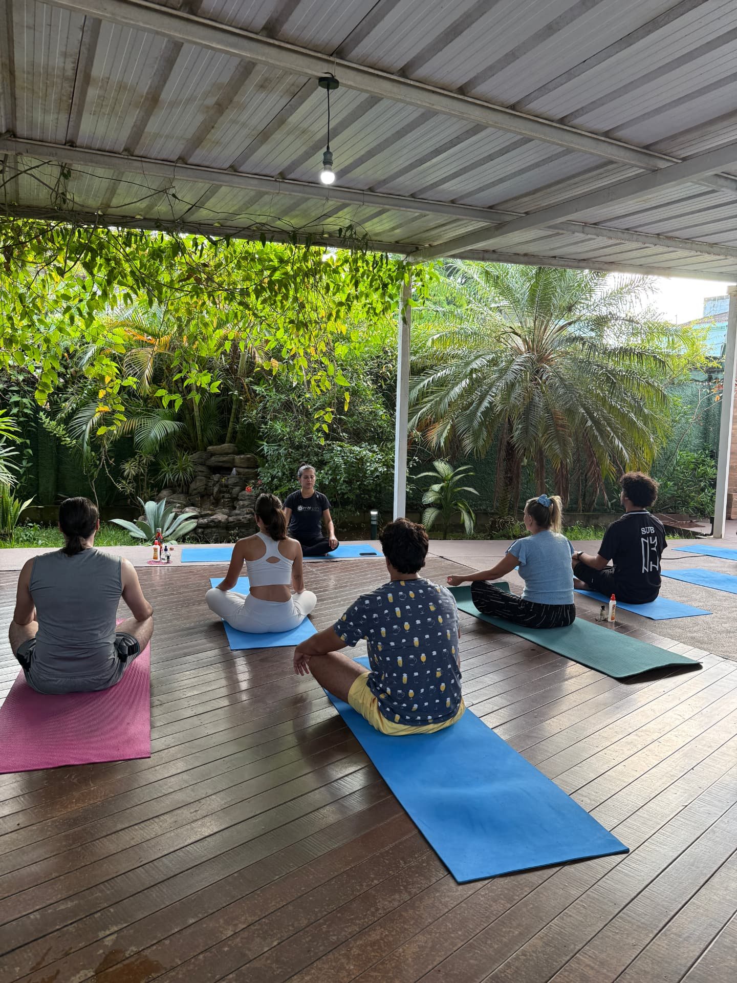 Aula de Yoga no deck do Marzen, com alunos em tapetes sob luz natural e jardim ao fundo